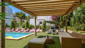 A covered outdoor area with a pool, lounge chairs, and a table with chairs.