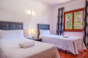 A hotel room with two beds, a nightstand, a lamp, and a window with curtains.