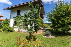 A white building with a sloped roof, surrounded by a well-maintained garden with various plants and a small pond.