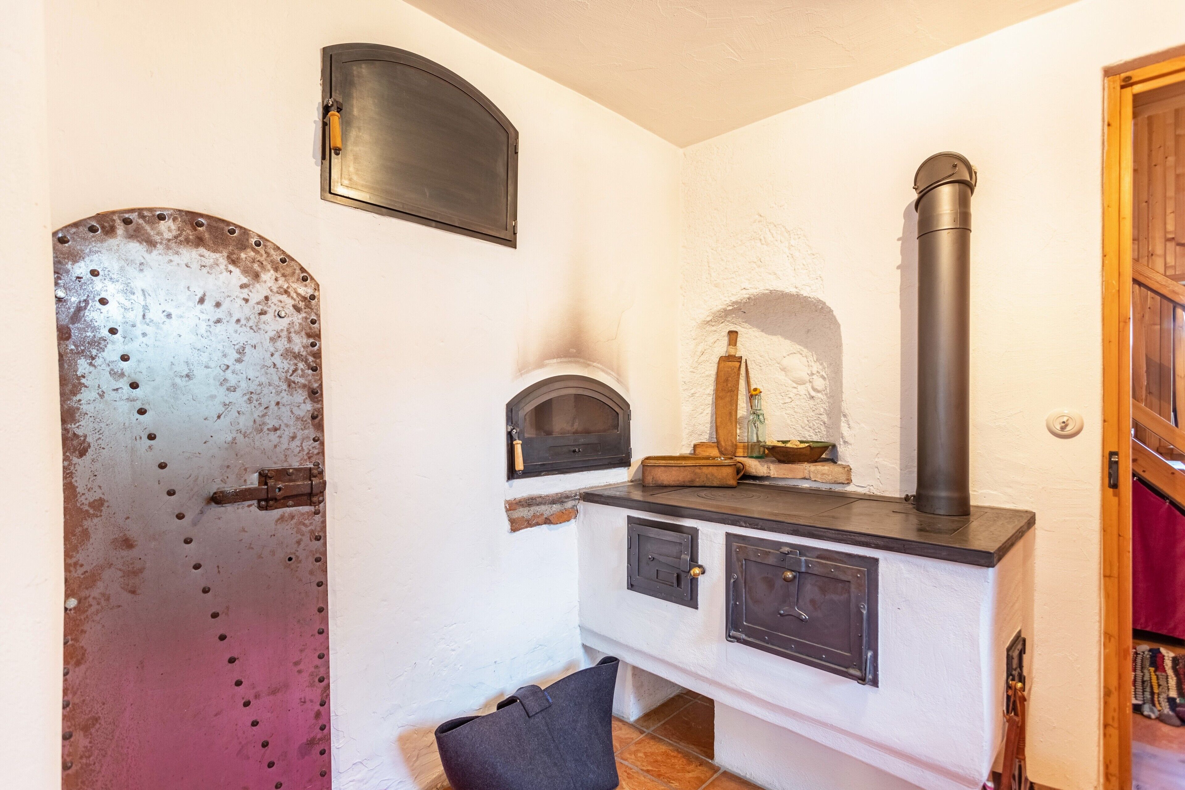 Une cuisine rustique avec un poêle à bois, une porte en métal et un petit four.
