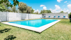 En rektangulär swimmingpool med ett vitt poolområde, omgiven av ett vitt staket och gräs.