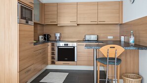Une cuisine compacte dotée de meubles en bois, d’un four encastré, d’un four à micro-ondes, d’une machine à café et d’un grille-pain.