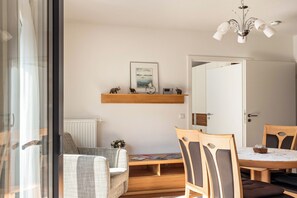 Ett modernt vardagsrum med en soffa, ett matbord med stolar, en öppen spis och en taklampa.