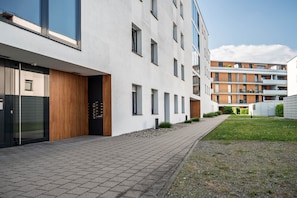 A modern building with a paved walkway, large windows, and a grassy area.