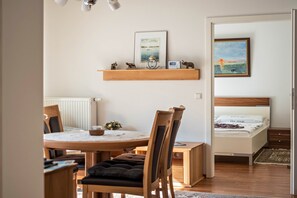 A cozy room with a wooden dining table, chairs, a bed with a headboard, a bedside table, and a shelf with decorative items.