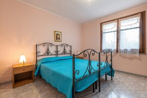 Une chambre à coucher avec un lit, une table de chevet, une lampe et une fenêtre avec des rideaux.