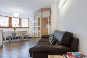 A modern living room with a leather sofa, a dining area with chairs, and a kitchen area with a window.