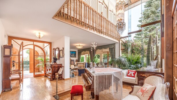 Amplia sala de estar con un piano de cola, una imponente escalera de madera y grandes ventanales con vistas al verdor.