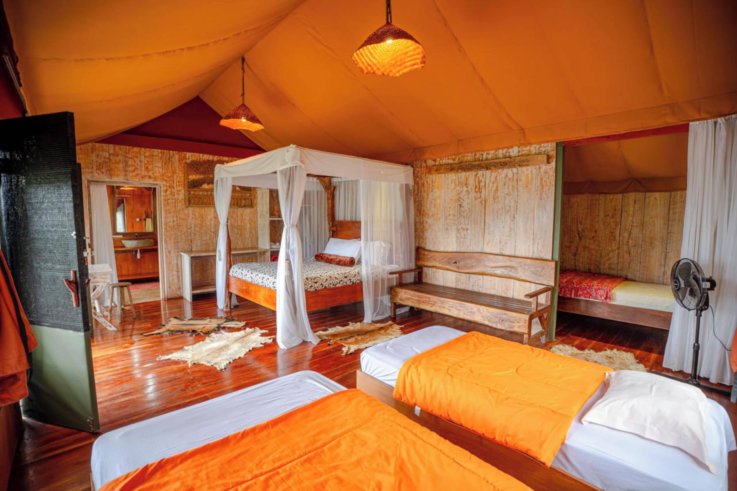 A tented accommodation with multiple beds, a wooden bench, and a fan.