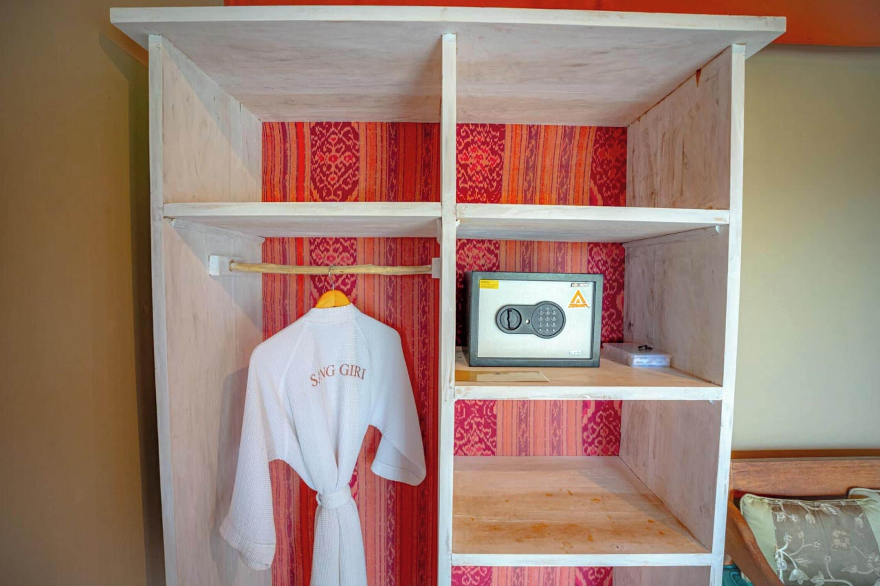 A wooden wardrobe with a red patterned interior, a white robe hanging on the door, and a radio on the top shelf.