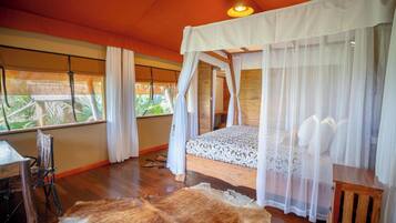 Un dormitorio con cama con dosel, piso de madera, vista a zonas verdes y un tapete de cuero rústico.