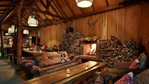 L’intérieur chaleureux d’un chalet avec une table à manger en bois, des bancs, un canapé agrémenté de coussins à motifs et une cheminée en pierre.