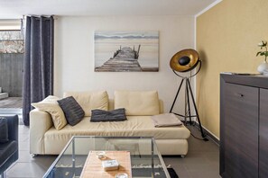 A living room with a sofa, a glass coffee table, a painting, a floor lamp, and a cabinet.