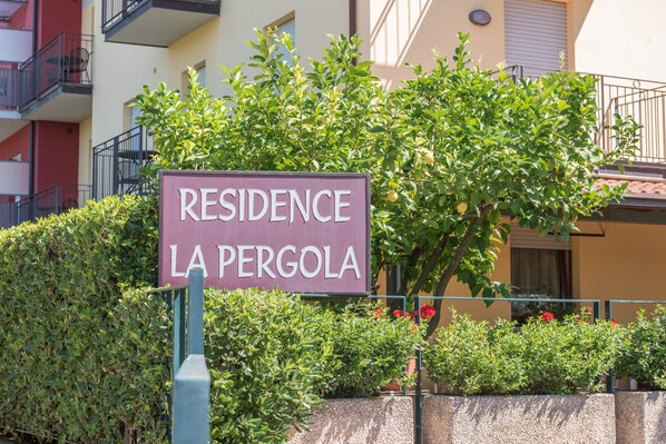 Naamplaatje voor 'Residence La Pergola', met een haag en een gebouw op de achtergrond.