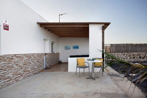Un espace patio avec un mur blanc, une partie inférieure en briques, un plafond en bois, une table avec deux chaises et une plante.