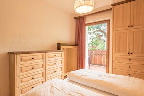A bedroom with two beds, wooden furniture, a window with a view of a balcony, and a ceiling light fixture.