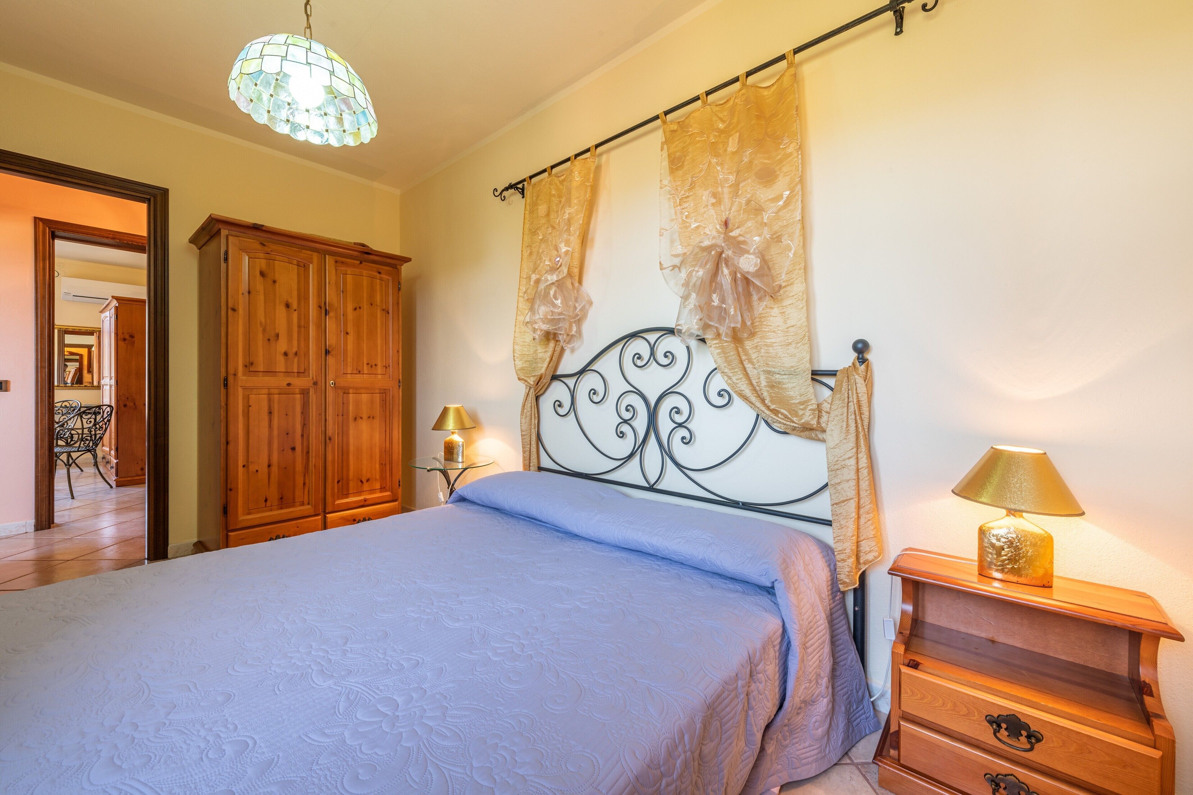 Ein Schlafzimmer mit einem Bett, einem Holzschrank, Vorhängen, einer Lampe und einer Chandelieber.