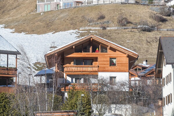 Un chalet en bois à deux étages, doté de balcons et entouré de collines enneigées.