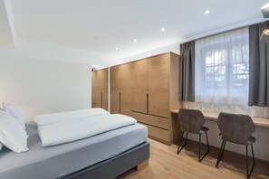 Un dormitorio moderno con cama, armario de madera y escritorio con sillas.