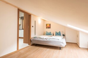 A bedroom with a bed, a wooden door, a wall-mounted light, and a small painting.