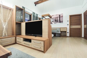 A modern living room with a flat-screen TV, wooden cabinets, and a dining area.
