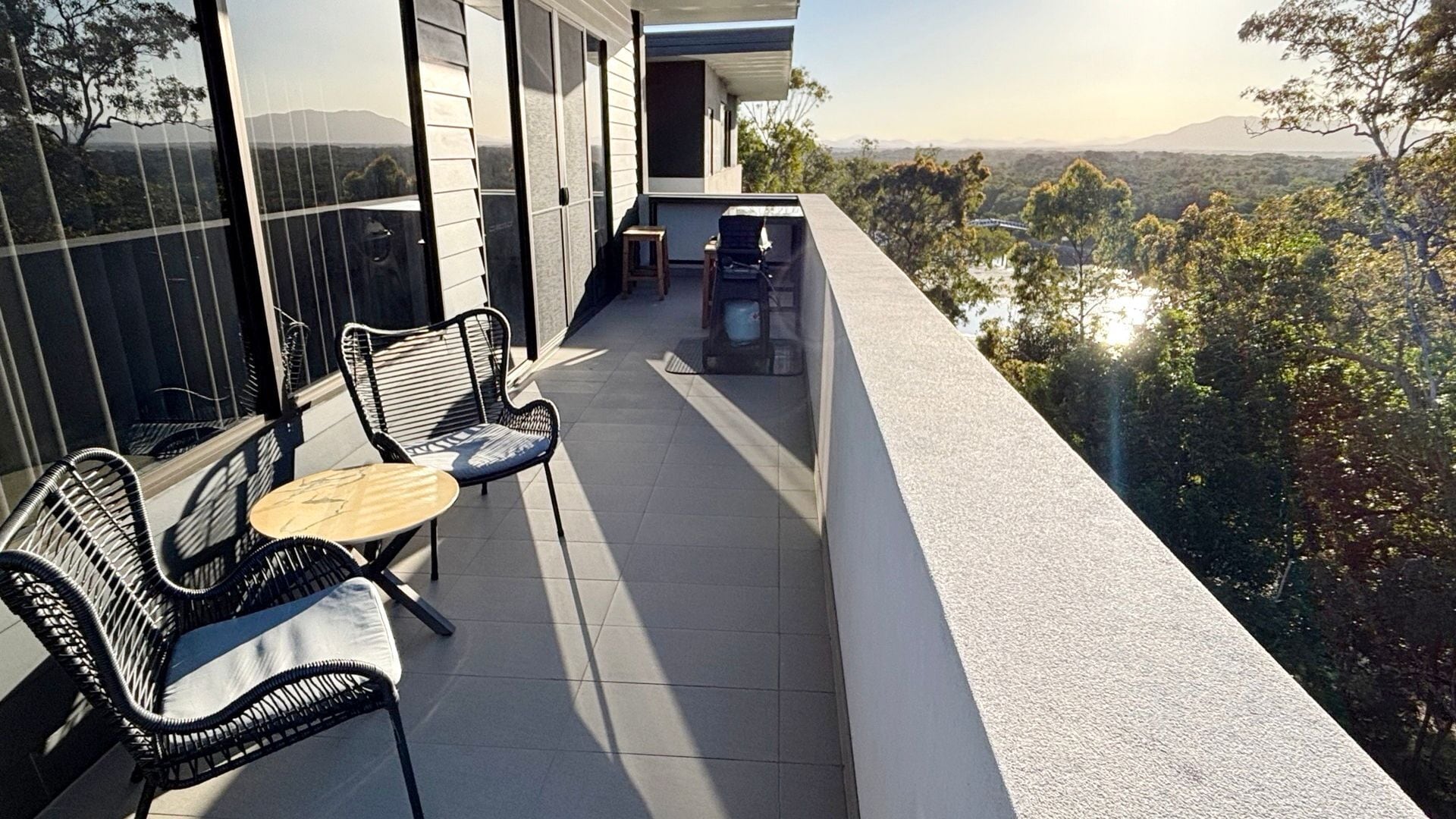 A balcony with two chairs and a small table, overlooking a scenic landscape with trees and hills.