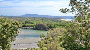 A coastal landscape with a beach, a calm lake, and a mountain range in the distance.