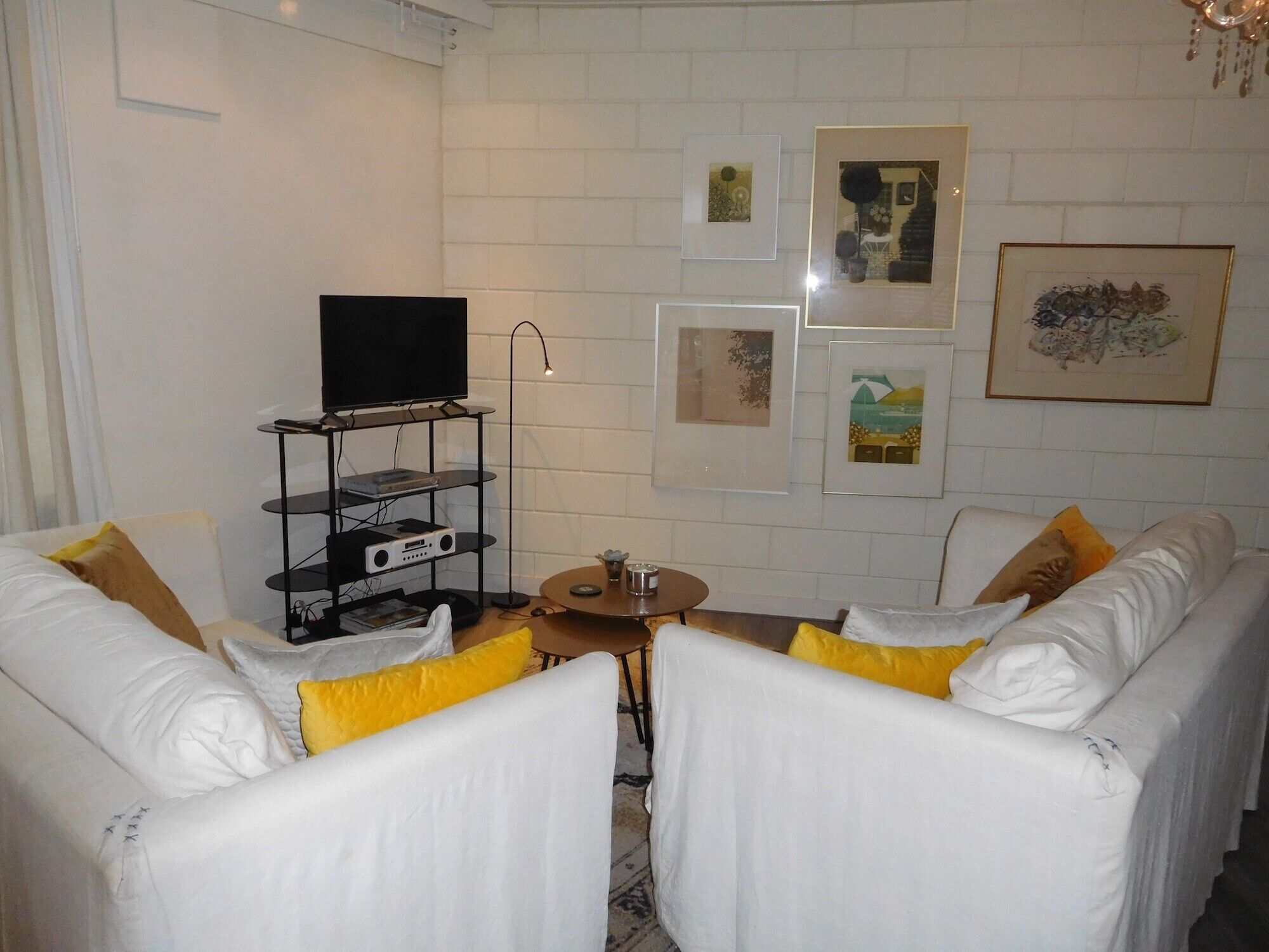 Un salon avec des canapés blancs, un téléviseur posé sur un meuble, une table basse et des œuvres d’art accrochées aux murs.
