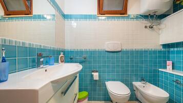 Un bagno con lavandino, water, bidet e piastrelle blu.