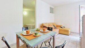 A dining area with a table set for two, a sofa in the background, and a view of a cityscape through a window. - Holiday Apartment "Il Nido" Near the Beach (Innamorata LI)