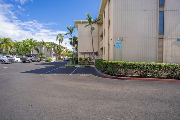 Un parking avec un bâtiment en arrière-plan, des palmiers et un ciel dégagé.