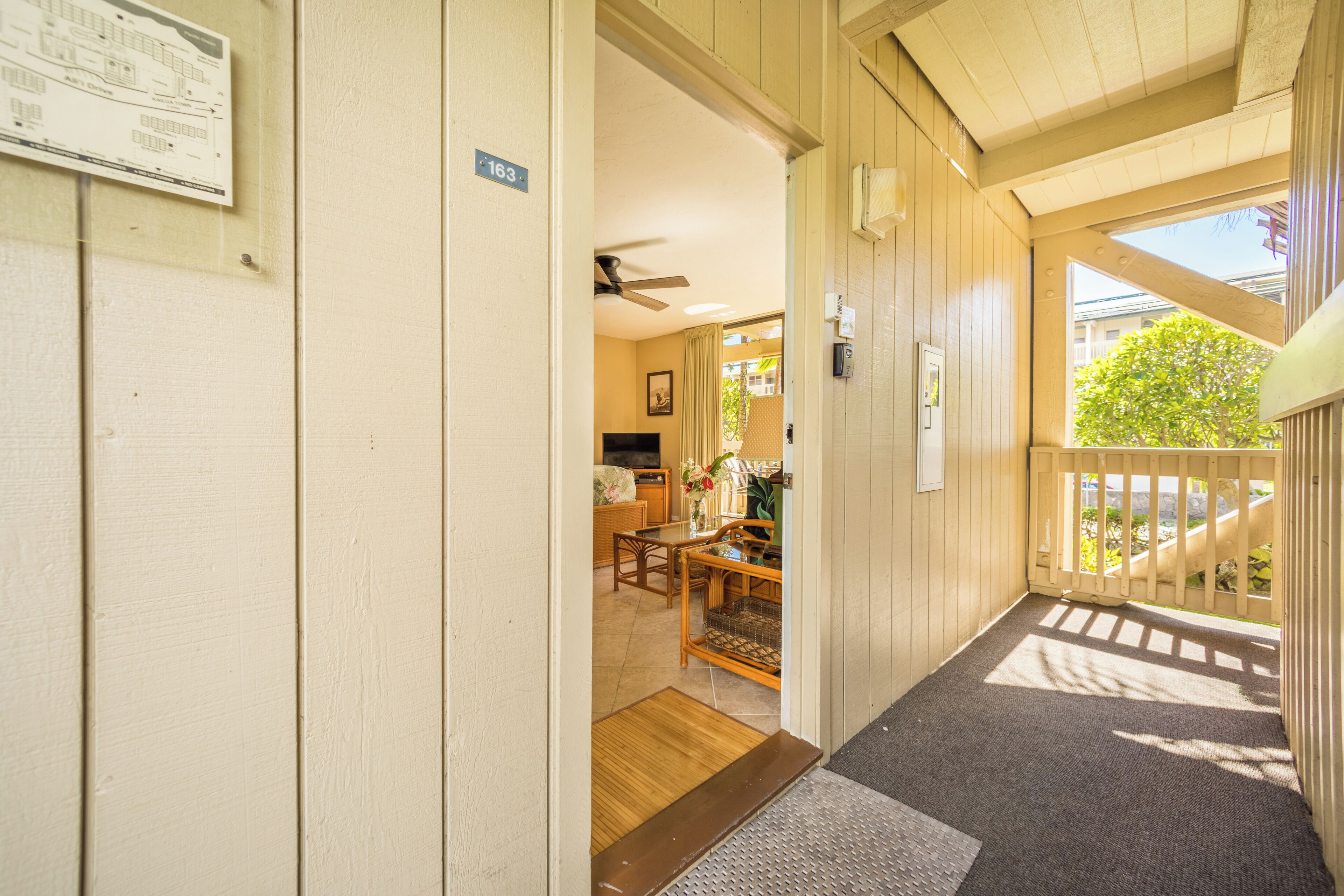 A hallway with a wooden door marked '163', a ceiling fan, and a view of a dining area with a table and chairs.