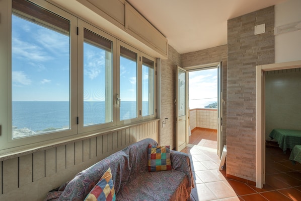 A room with a view of the sea, a sofa with a patterned cover, and a door leading to a balcony. - Cosy Home Minutes From Seaside - Casa Vacanza Marina (MARINA DI ANDRANO)