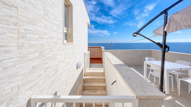 Un bâtiment moderne à la façade blanche, avec un escalier menant à un balcon et une vue sur la mer.