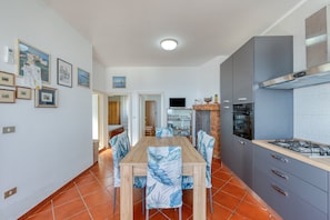 A modern kitchen with grey cabinets, a wooden dining table, and blue chairs. - Cosy Home Minutes From Seaside - Casa Vacanza Marina (MARINA DI ANDRANO)