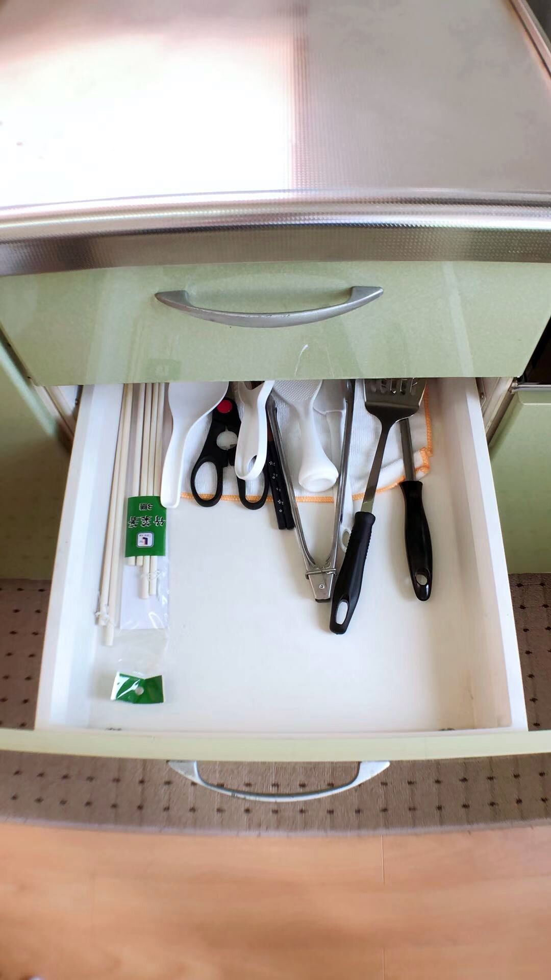 A drawer with various kitchen utensils including scissors, a spatula, and chopsticks.