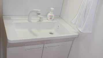 A small, white bathroom with a sink, a mirror, a towel rack, and a small shelf above the sink.
