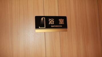 A black and gold bathroom sign with a shower icon and the word 'BATHROOM' in English and another language.