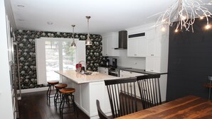 A modern kitchen with white cabinetry, a wooden dining table, and bar stools. - Luxury Cottage on ice-fishing Rice Lake and year round activities (Bewdley)