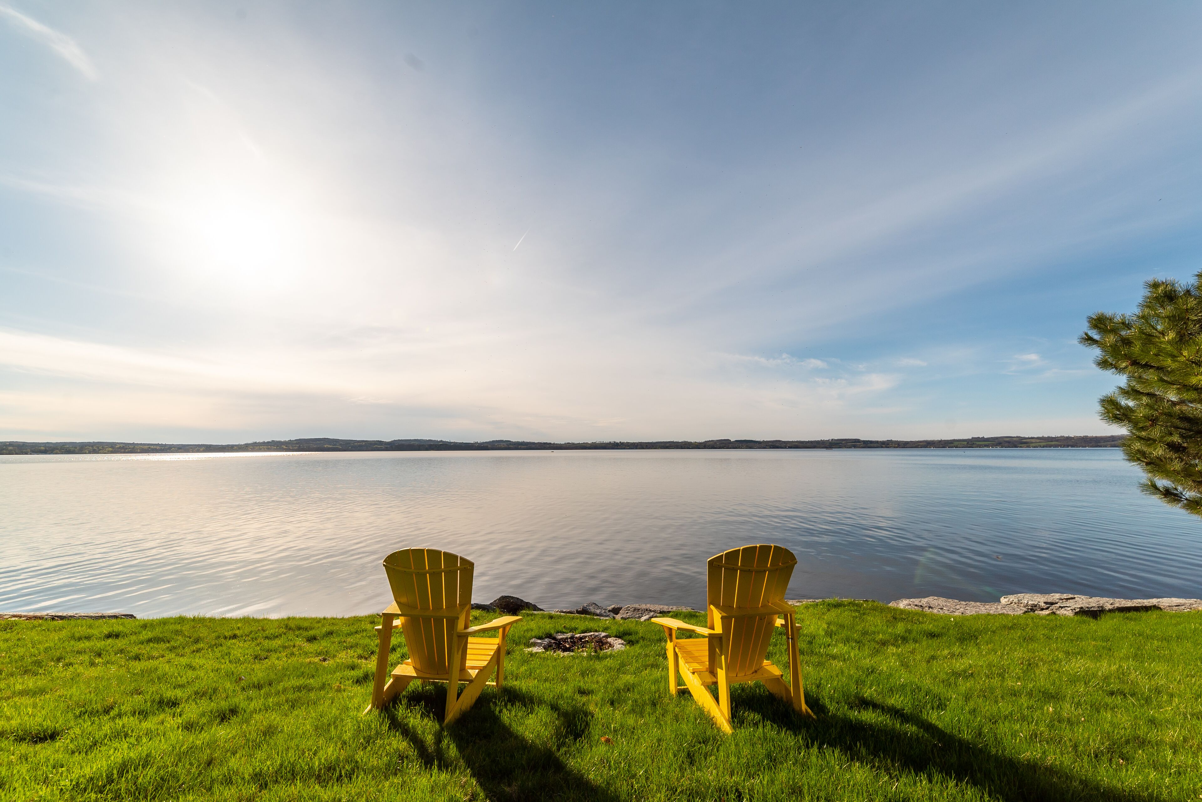 Two yellow Adirondack chairs facing a calm lake with a clear sky.