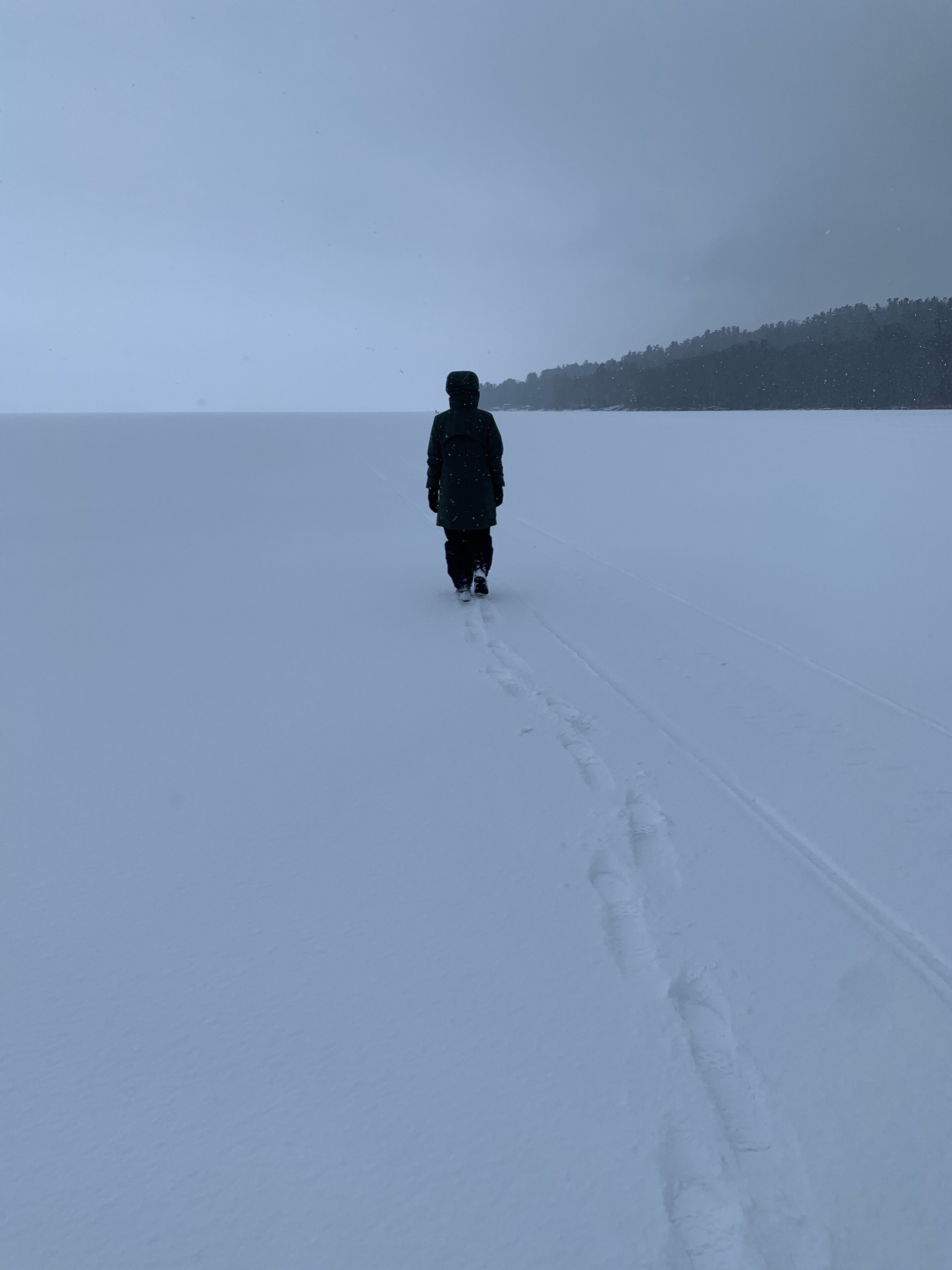 Une personne marchant sur un sentier enneigé, où l’on peut voir des empreintes de pas.