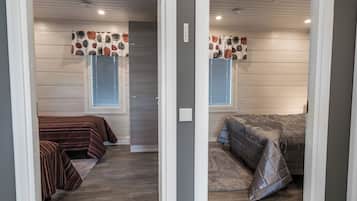 A room with two beds, a window with blinds, a ceiling with recessed lighting, and a door with a sign.