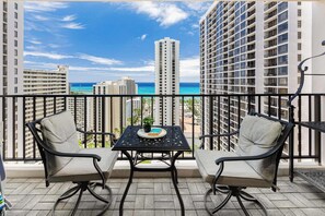 A balcony with two chairs, a table, and a view of the ocean and buildings. - Ocean-view corner suite w/ pool & parking (Honolulu)
