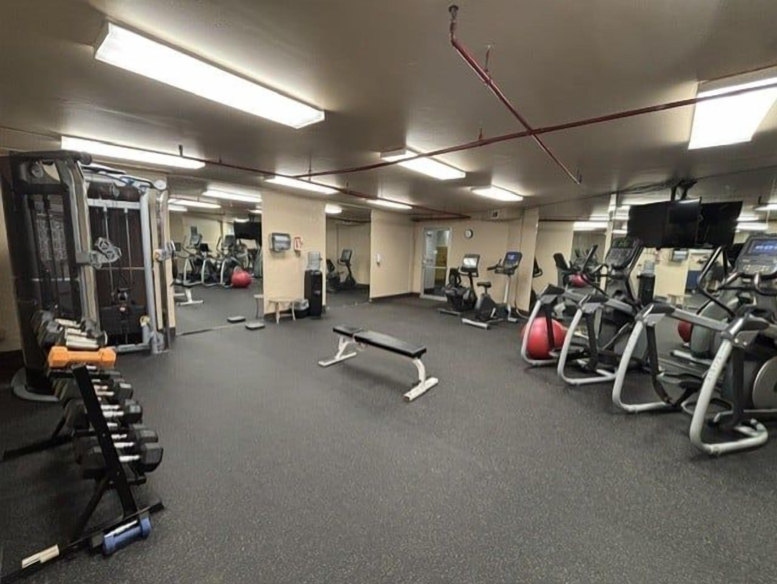 Een fitnessruimte met cardioapparatuur, gewichthefmaterialen en spiegels.