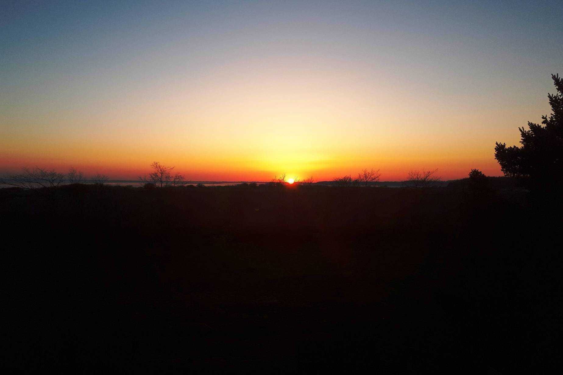 A sunset over a flat landscape with sparse vegetation.