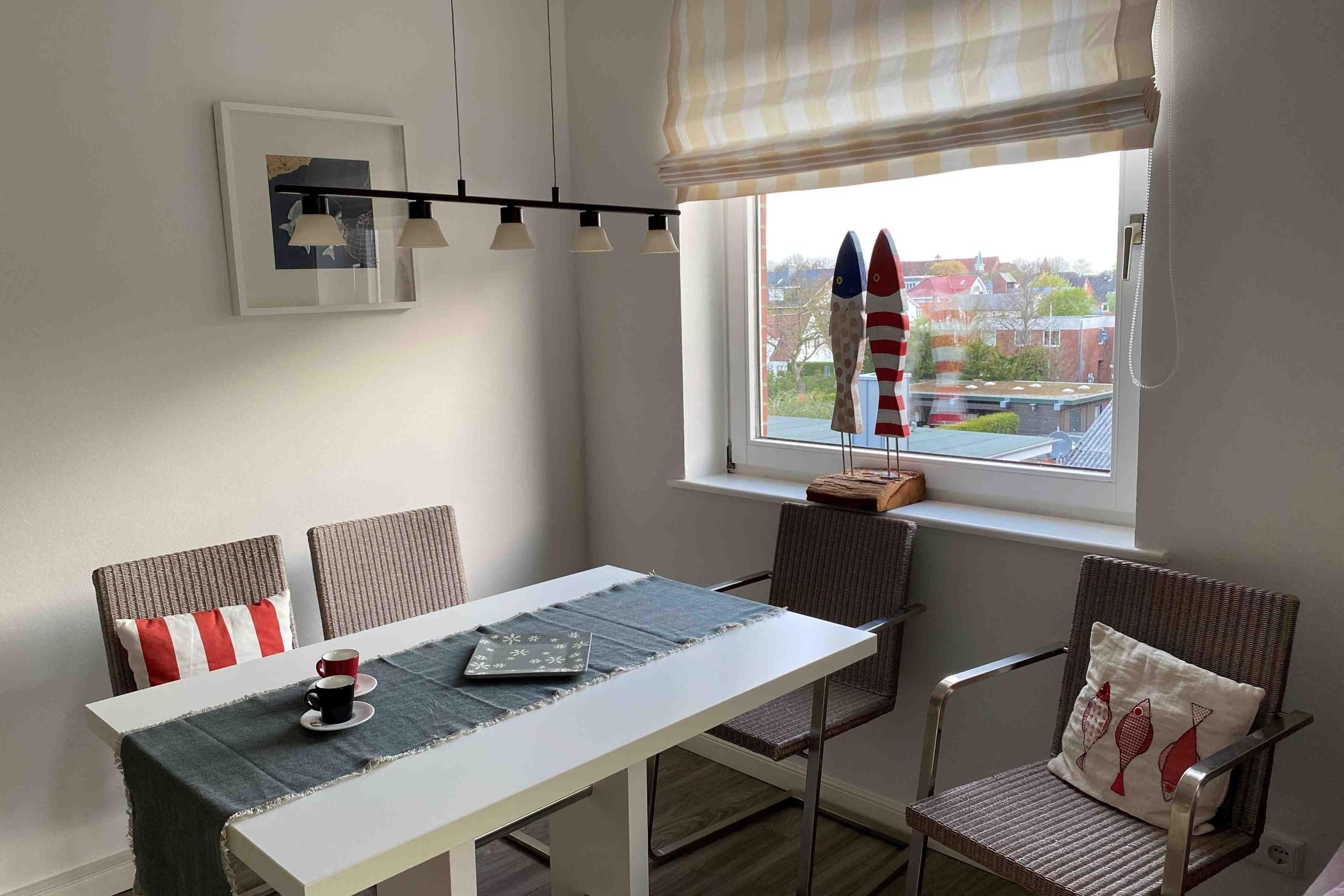 A dining area with a white table, two chairs, a table runner, and a framed picture on the wall.
