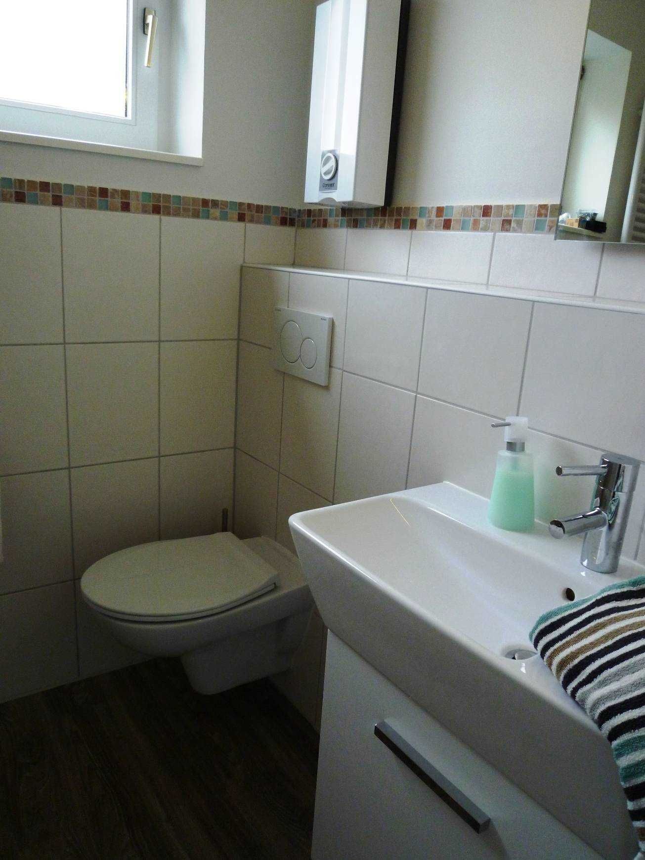 Ein Badezimmer mit Toilette, einem Waschbecken mit Seifenspender, einem Spiegel und einem Fenster.