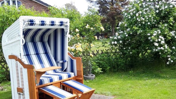 A wicker lounge chair with striped cushions in a garden setting. - Feer Strunhüs Deelswai 49 (Nieblum)