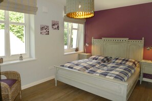 A bedroom with a white bed, purple walls, and a window with a view of trees.