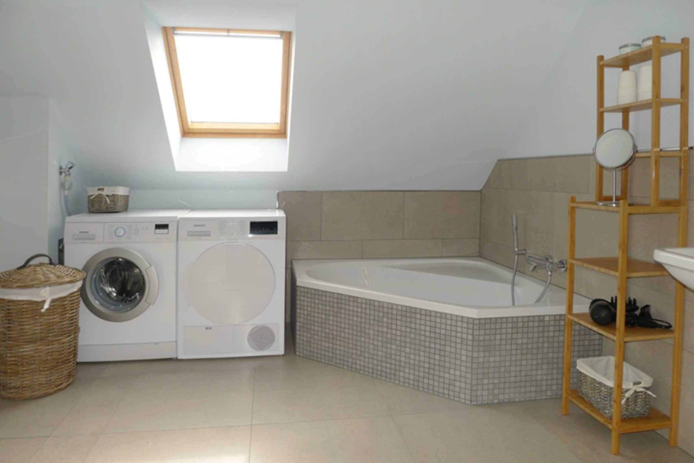 Un espace buanderie équipé d’un lave-linge et d’un sèche-linge, une baignoire d’angle et une étagère en bois avec des bocaux.